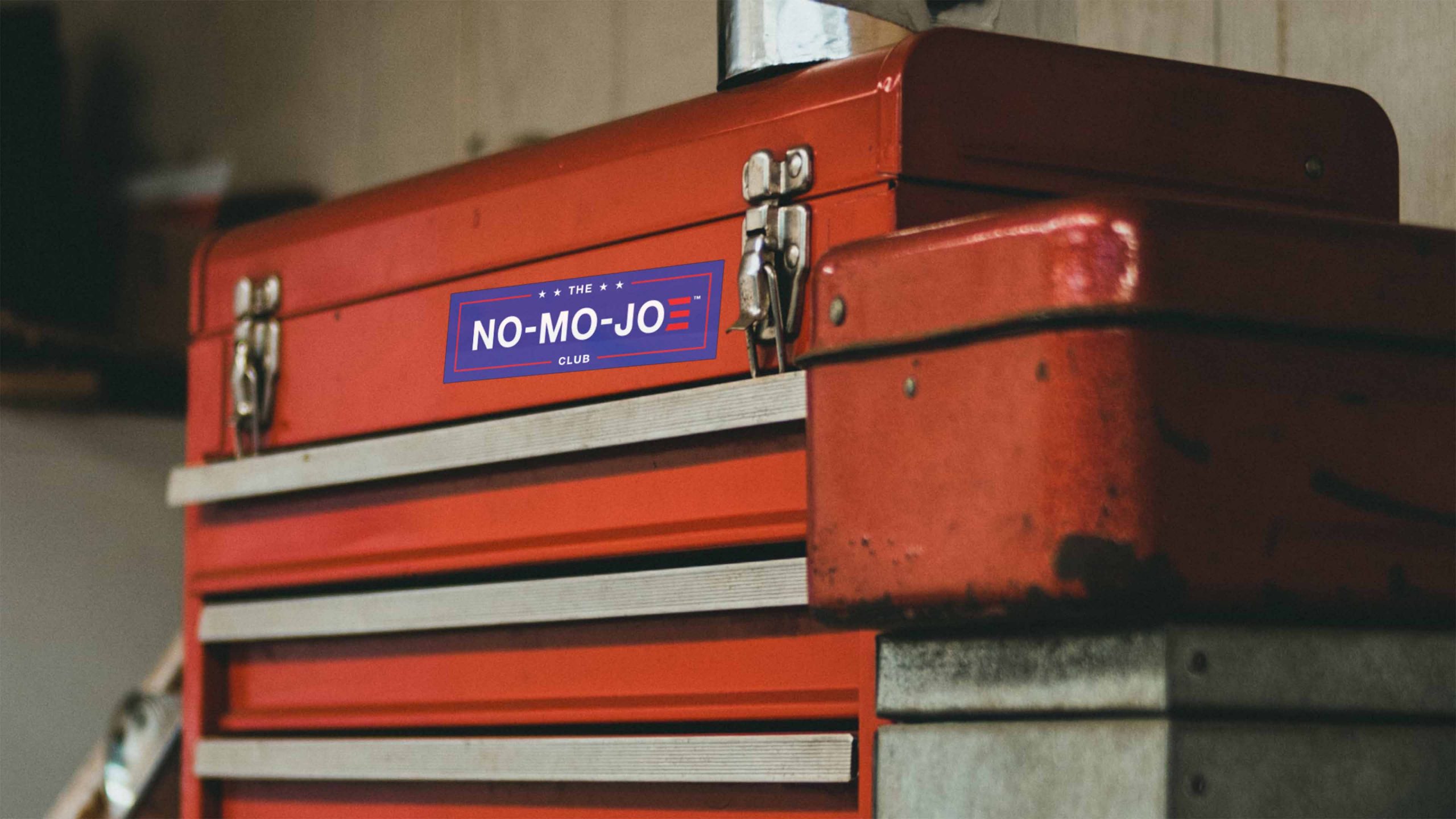 The No-Mo-Joe Club™ sticker on hood of multidrawer red tool box in shop.