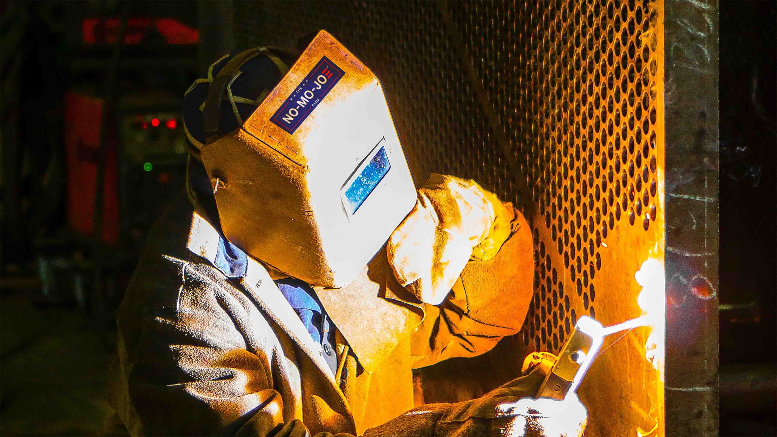 The No-Mo-Joe Club™ sticker on top of welders face shield as he works with sparks and flame