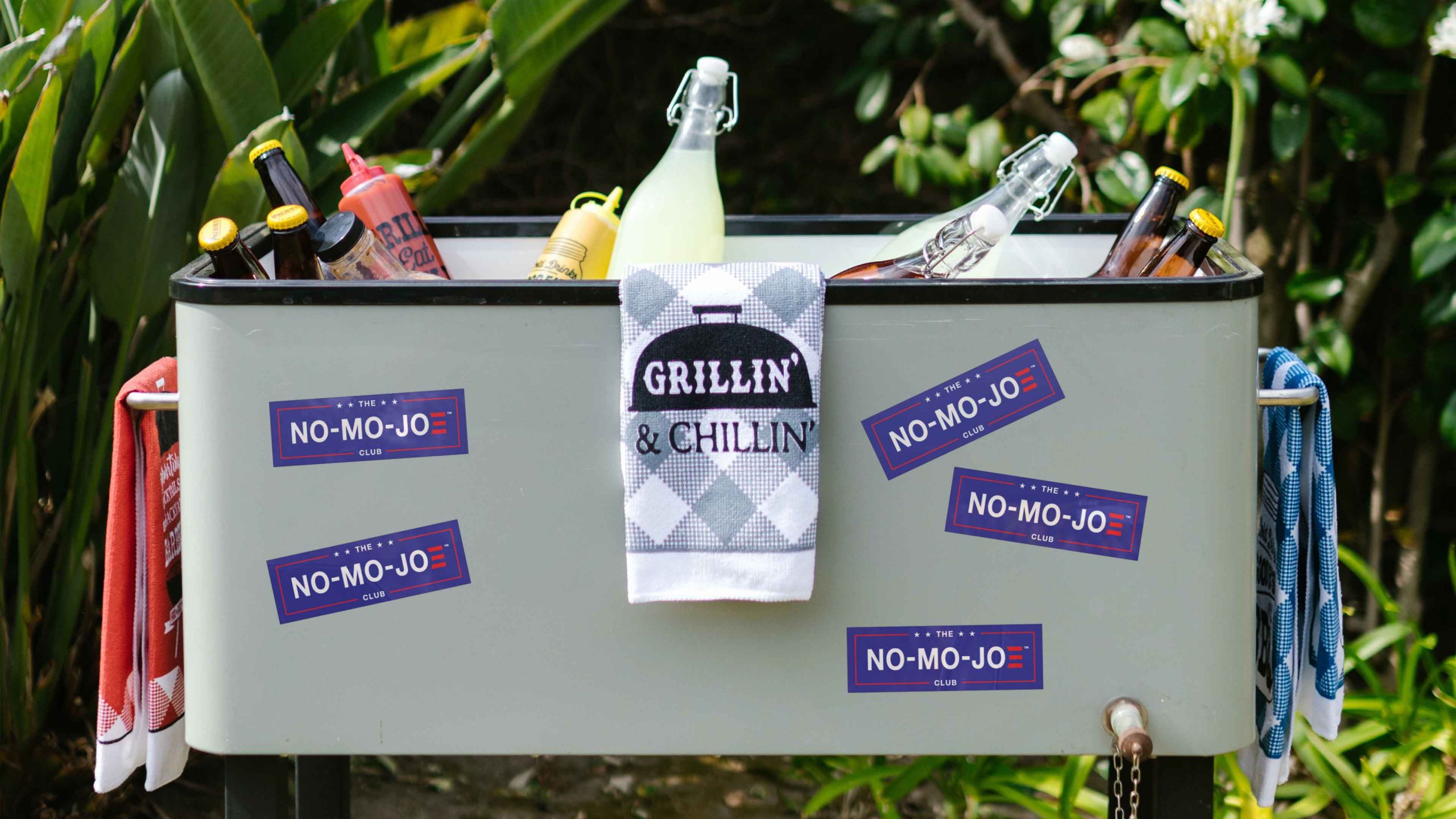 The No-Mo-Joe Club™ stickers covering cooler with bar towels and assorted beverages and condiments inside.